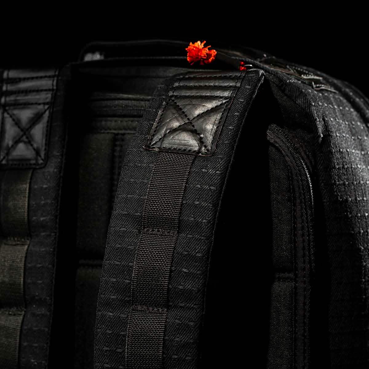 Close-up of a black GR1 USA x Carryology - GRXC2 Samurai backpack strap, crafted from Japanese cotton, with a small red flower on top against a black background.