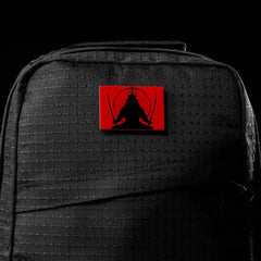 The GR1 USA x Carryology - GRXC2 Samurai is a black backpack made from durable Japanese cotton, featuring a red patch with a samurai wielding two swords.