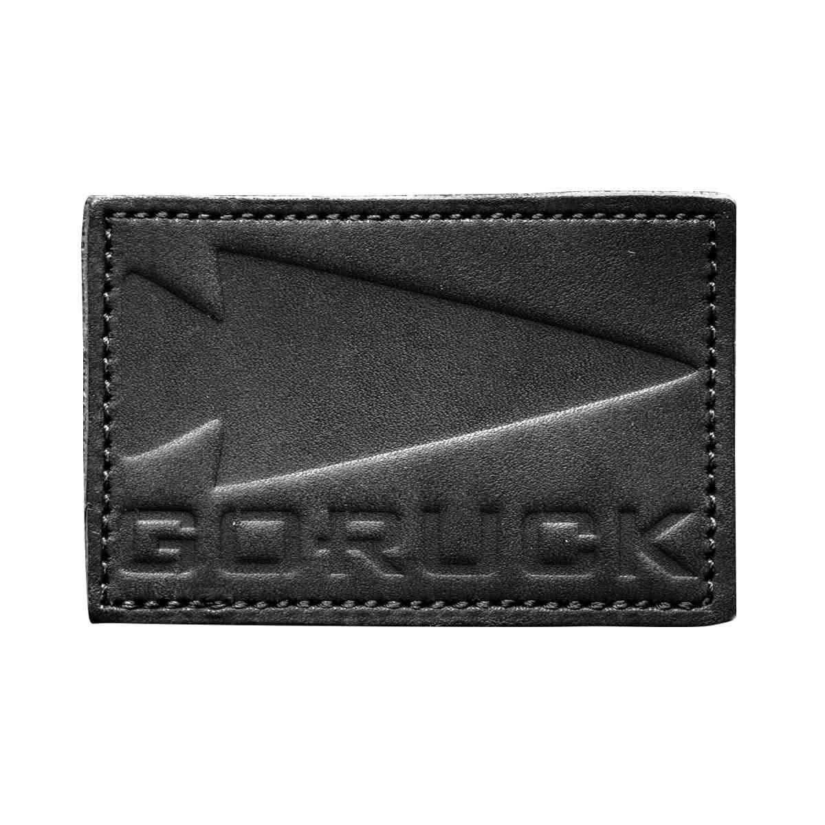 The Patch - Leather GORUCK Spearhead from vendor-unknown is made from black full-grain cowhide leather and features an arrow embossed alongside the text "GORUCK." It has visible stitching along the edges, a slightly textured surface, and comes with a VELCRO® backing for easy attachment.