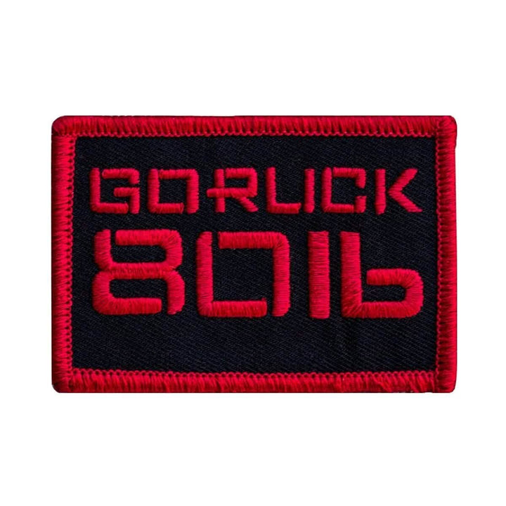 Introducing the Patch - Sandbag Weight by vendor-unknown: a rectangular design with a striking black background and red border, ideal for rucksacks. It showcases the embroidered text GORUCK 8016 in vibrant red and attaches easily using secure VELCRO strips.