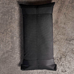 The GORUCK Sandbags 2.0, with their simple and sturdy design, lay on a rough-textured gray concrete floor in a top-down view. This rectangular black weighted bag, made from rugged 1000D CORDURA, showcases visible seams and reinforced corners, making it ideal for training sandbags.