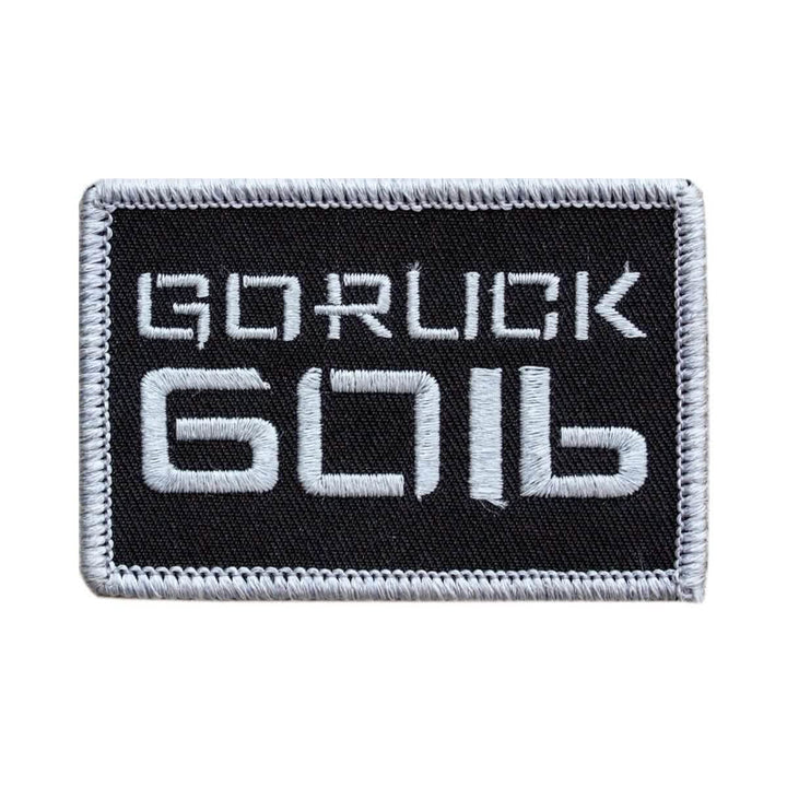 Product Description: The Patch - Sandbag Weight by vendor-unknown features a black rectangular design with a white border. The bold, stylized "GORUCK 6016" text is embroidered on the patch. It includes a VELCRO backing, making it ideal for attaching to rucksacks or sandbags, and it boasts a clean and minimalist aesthetic.