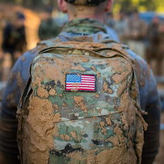 The back of a man in a military uniform with mud splattered over a patch featuring the American Flag by vendor-unknown.