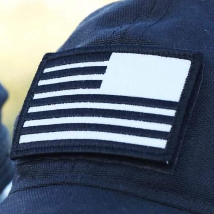 The image shows a close-up of the "Patch - Reflective Reverse Flag" by vendor-unknown, featuring an embroidered monochrome American flag with black and white stripes and stars on a dark fabric background, complete with a VELCRO backing for easy attachment.