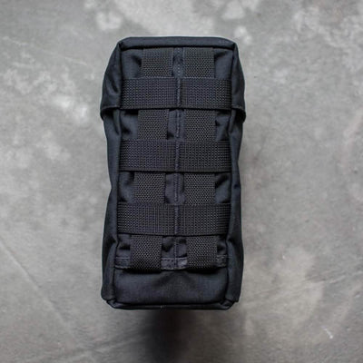 The image features the GORUCK Full Panel Water Bottle Pocket, a black tactical pouch with a MOLLE attachment system, positioned vertically on a textured gray surface. The pouch is sturdy and compact, ideal for attaching to outdoor gear or backpacks.