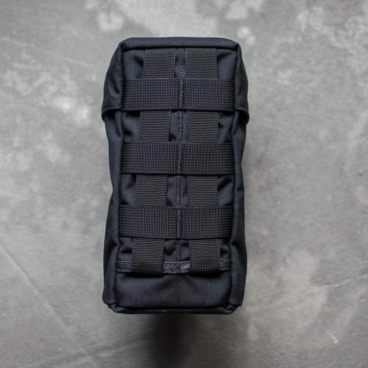 The image features the GORUCK Full Panel Water Bottle Pocket, a black tactical pouch with a MOLLE attachment system, positioned vertically on a textured gray surface. The pouch is sturdy and compact, ideal for attaching to outdoor gear or backpacks.