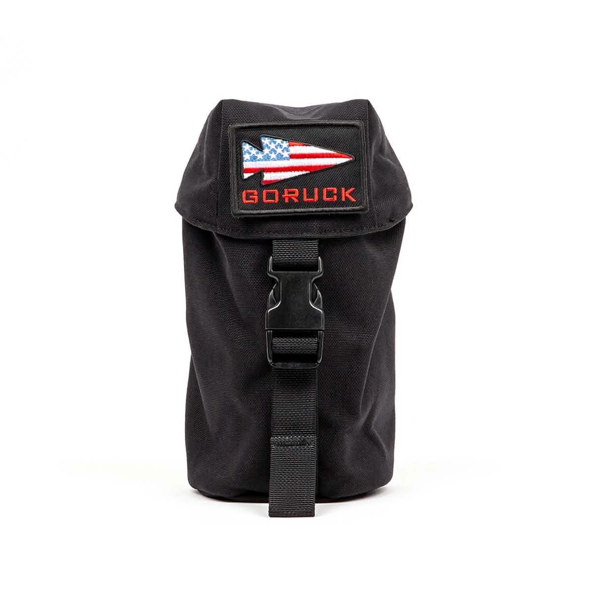 The Full Panel Water Bottle Pocket from GORUCK is a black pouch with a buckle closure and MOLLE attachment system. It includes a patch with an American flag design and the text "GORUCK" in red. The pouch, standing upright against a plain white background, is perfect for securely carrying essentials like a Nalgene-style water bottle.