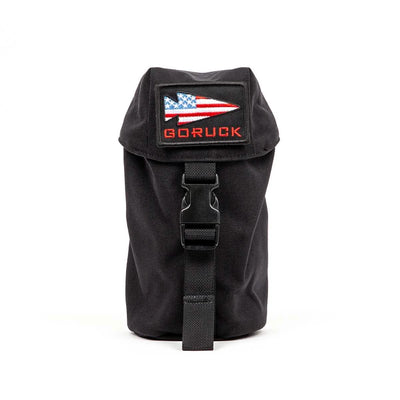 The Full Panel Water Bottle Pocket from GORUCK is a black pouch with a buckle closure and MOLLE attachment system. It includes a patch with an American flag design and the text "GORUCK" in red. The pouch, standing upright against a plain white background, is perfect for securely carrying essentials like a Nalgene-style water bottle.
