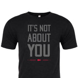 The "It's Not About You" T-shirt features bold gray text and a red arrow on black, crafted from premium tri-blend fabric. Proudly printed in the USA for comfort and style.