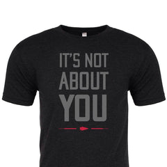 The "It's Not About You" T-shirt features bold gray text and a red arrow on black, crafted from premium tri-blend fabric. Proudly printed in the USA for comfort and style.
