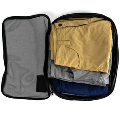 Open packing cube with folded khaki, gray, and blue rucking pants inside against white background