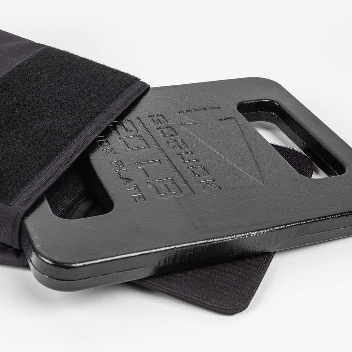 A close-up shot features a black, rectangular GORUCK Ruck Plate partially inserted into a pouch. The plate bears text indicating it weighs 20 pounds, highlighting the robustness of American manufacturing. The backdrop is plain white.