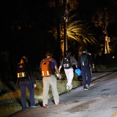Four people rucking at night on a street, wearing GORUCK backpacks with reflective bands under palm trees