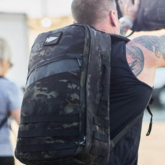 GORUCK camo rucksack with reflective spearhead patch worn by man at outdoor fitness event