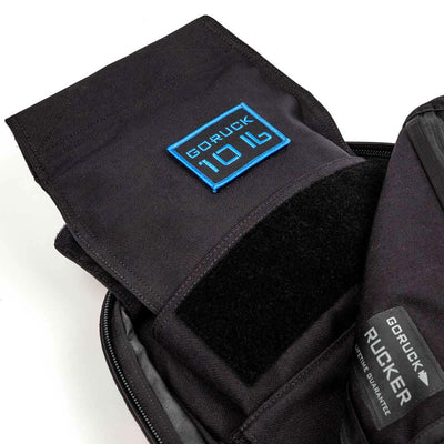 Close-up of a black GORUCK Ruck Sandbag - 10LB showcasing its interior. The flap is open, revealing the GORUCK logo stitching in blue and a patch displaying 10LB on fabric. VELCRO® closures and zippers enhance the construction, embodying attention to detail suitable for carrying your Ruck Plate securely.