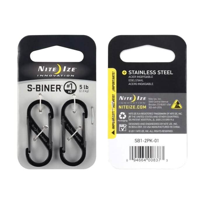 Packaging for the Nite Ize Carabiner - Hydration Bladder Attachment, ideal for securing to your rucksack. The front displays two black carabiners designed to support up to 5 lbs each. The back includes product information, usage warnings, and a barcode. These carabiners are crafted from durable stainless steel.
