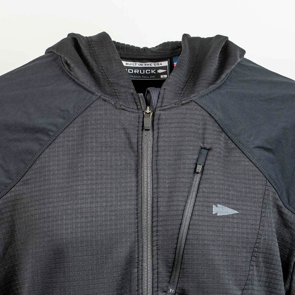 A close-up of the Men’s Full Zip - Polartec Grid Fleece by GORUCK highlights its Polartec Power Grid material, featuring a hood and multiple zippers. The chest is adorned with a small arrow logo, while the tag inside the collar is visible. The textured grid pattern suggests its sturdy ToughDry Fabric construction.
