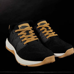 Introducing the Men's Ballistic Trainers in Black, White, and Coyote by GORUCK: a pair of sleek athletic shoes that combine black uppers with tan laces and soles designed for functional fitness footwear. These trainers are set against a plain black background, featuring slightly elevated soles crafted from engineered warp knit and synthetic fabric for enhanced durability.
