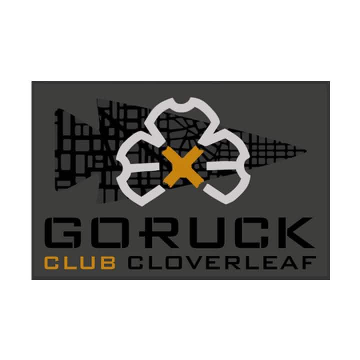 Patch for the GORUCK Ruck Club Cloverleaf showcasing a stylized cloverleaf design intersected by a yellow X on a dark background. The bold lettering spells out 