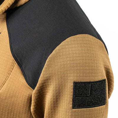 Close-up of a brown Men’s Half Zip - Polartec Grid Fleece by GORUCK, featuring a black shoulder panel and a rectangular Velcro patch on the sleeve. Crafted with ToughDry Fabric, its detailed weave pattern is visible, highlighting the jacket's durability and style.