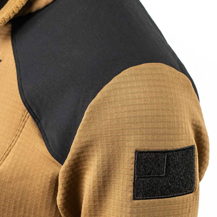 Close-up of a brown Men’s Half Zip - Polartec Grid Fleece by GORUCK, featuring a black shoulder panel and a rectangular Velcro patch on the sleeve. Crafted with ToughDry Fabric, its detailed weave pattern is visible, highlighting the jacket's durability and style.