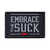 GORUCK black embroidered patch with gray 'Embrace the Suck' text and red arrow accent.