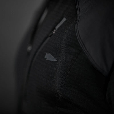 Close-up of a person wearing the Men’s Half Zip - Polartec Grid Fleece by GORUCK, featuring a small, triangular logo on the black fabric. The ToughDry Fabric showcases a textured pattern, and the shirt includes a front zipper. The background is dark gray.