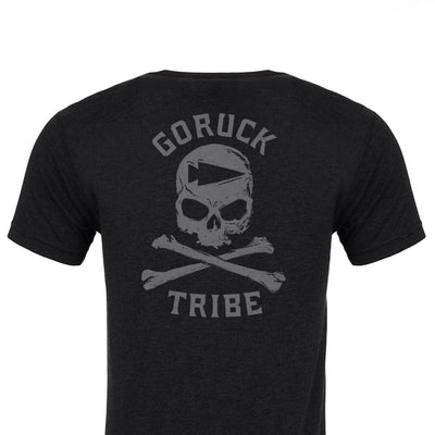 A GORUCK Tribe Tee - Tri-Blend in black showcases a striking design on the back, featuring a skull and crossed bones. "GORUCK Challenge" is prominently displayed above, with "TRIBE" printed below, encapsulating the essence of shared pain and unity inherent in every GORUCK Tribe adventure.