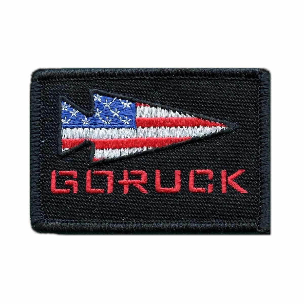 Rectangular embroidered patch from vendor-unknown, aptly named "Patch - GORUCK USA," features a black background with the GORUCK spearhead design—a stylized arrowhead adorned with an American flag pattern. The word "GORUCK" is prominently embroidered in bold red capital letters beneath it, paying tribute to its Special Forces connection.