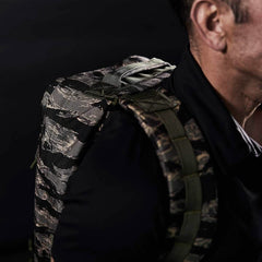 Close-up of a person wearing the GR1 - USA - Tiger Stripe rucksack, featuring a bold camouflage pattern inspired by the iconic Special Forces backpack, against a dark background.