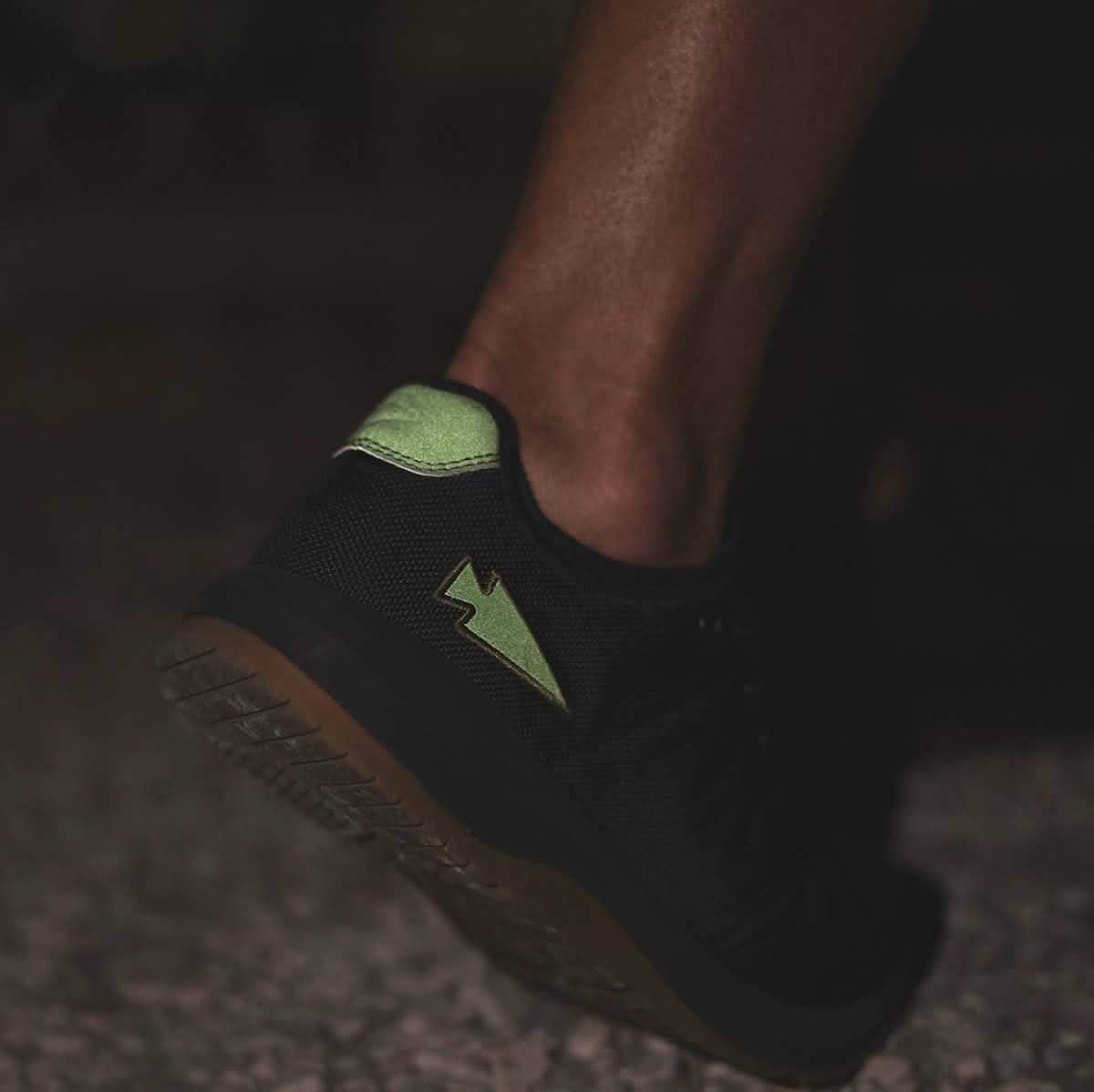 Close-up of a person wearing Ballistic Trainers - Black + Gum w/ Green Reflective Spearhead, featuring durable CORDURA Ballistic Nylon and green reflective spearhead logo for lasting functional fitness.