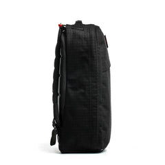 Side view of the black GR1 USA x Carryology - GRXC2 Samurai backpack with a zipper and minimal design, made from premium Japanese cotton, standing upright on a white background.