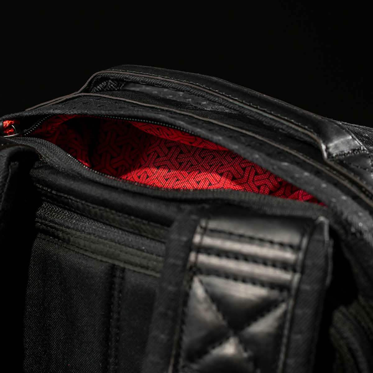 Close-up of the GR1 USA x Carryology - GRXC2 Samurai bag, showing its red patterned Japanese cotton fabric lining through the partially unzipped black exterior.