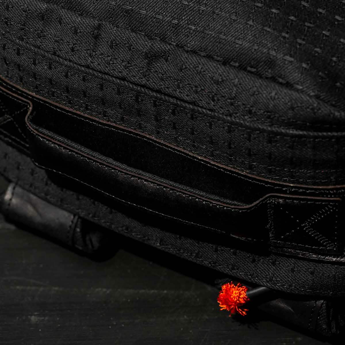 Close-up of the black GR1 USA x Carryology - GRXC2 Samurai bag, crafted from Japanese cotton with a textured finish and an orange tassel detail at the bottom right corner.
