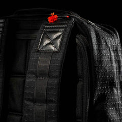 Close-up of the GR1 USA x Carryology - GRXC2 Samurai backpack, crafted with Japanese cotton, featuring a small red flower tucked under one shoulder strap against a black background.