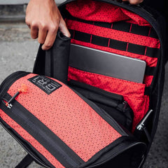 A hand opens the GR1 USA x Carryology - GRXC2 Samurai backpack, revealing a red Japanese cotton fabric interior and a laptop inside its padded compartment.