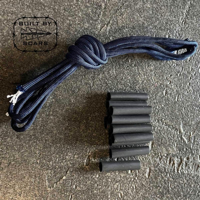 A coiled black paracord and several black cylindrical sleeves, much like heat shrink tubes, are laid out on a textured dark surface. In the top left corner is a logo featuring "BUILT BY SCARS" with a knife graphic, ideal for your next DIY ruck upgrade project.