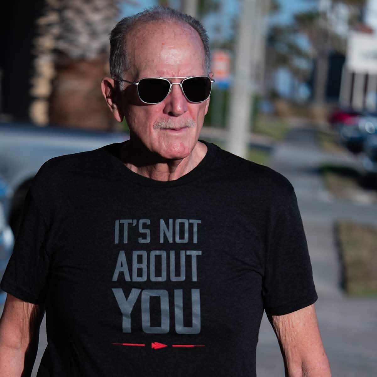 An older man in sunglasses walks outdoors on a sunny day wearing the 