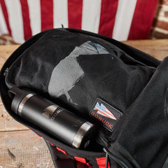 GORUCK packing cube inside backpack with black water bottle, wooden table and American flag backdrop