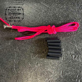 Bright pink paracord and black heat shrink tubes on textured surface, GORUCK gear accessory.