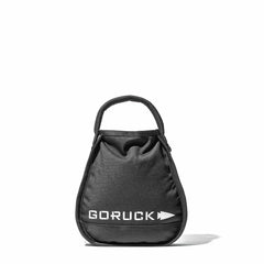 A Sand Kettlebell by GORUCK, featuring a black bag with the brand's name and an arrow logo printed in white, highlights an endurance design. The product resembles a portable sand kettlebell with a strong handle on top and is displayed against a plain white background.