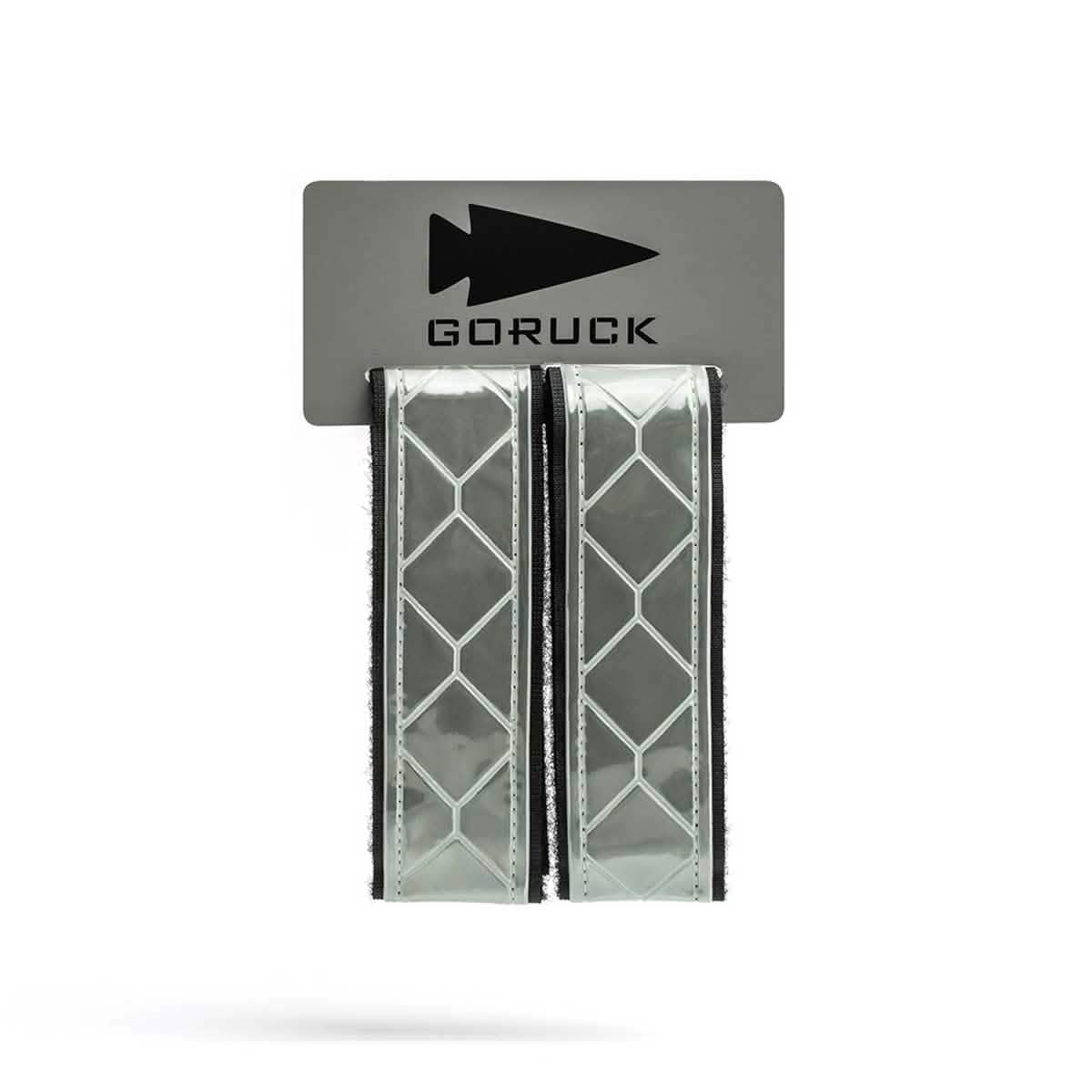 The GORUCK Reflective Ruck Bands, showcasing a diamond pattern, are affixed to a gray card emblazoned with the arrowhead logo and the brand name. Equipped with MOLLE webbing for secure attachment, these bands improve nighttime visibility, enhancing safety during outdoor activities.